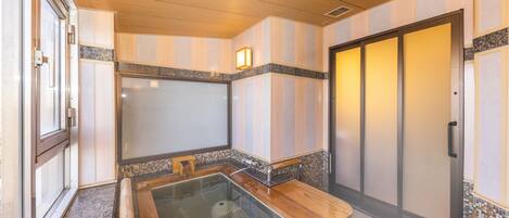 A modern bathroom with a glass-enclosed hot tub, wooden flooring, and a sliding door.