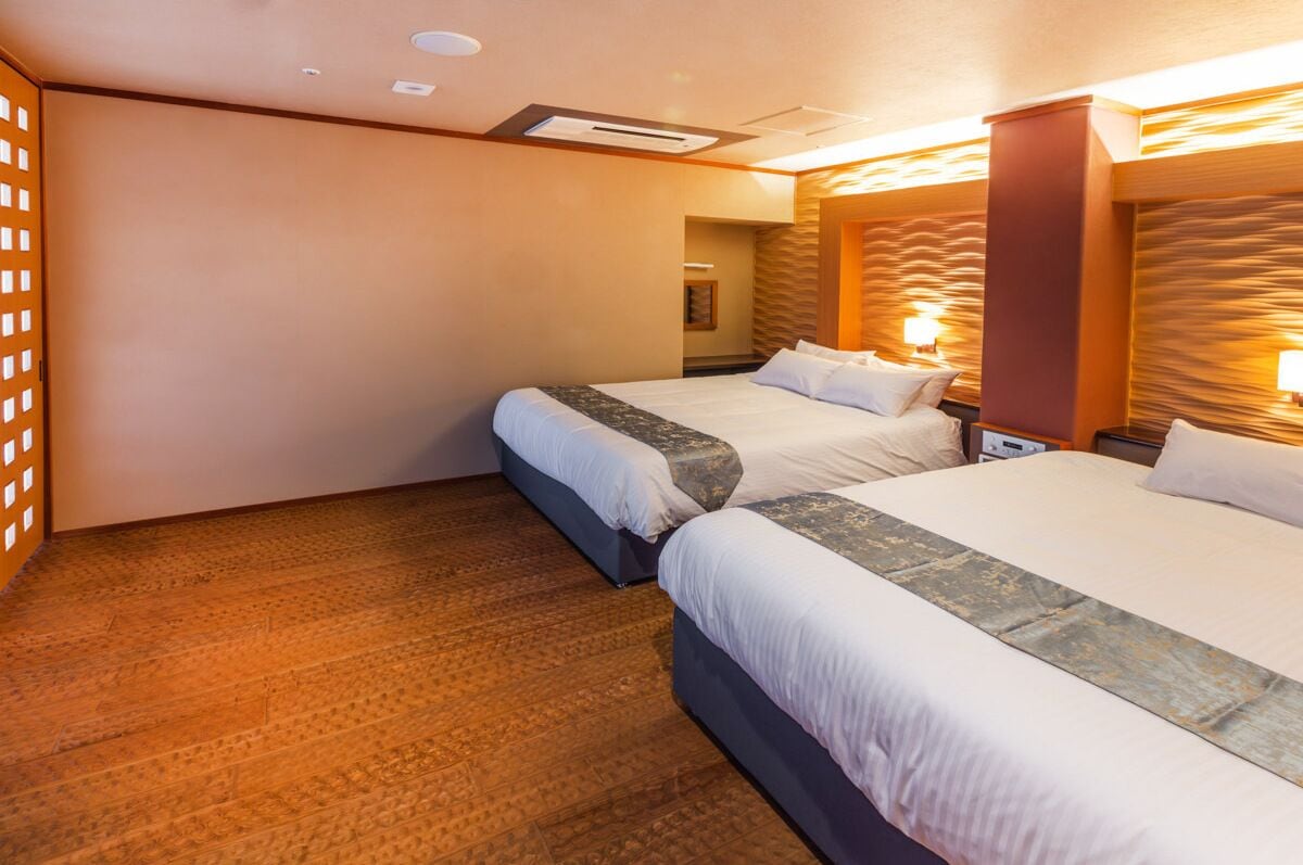 A hotel room with two beds, wooden flooring, and a modern design with a warm color scheme.