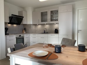 A modern kitchen with white cabinets, a built-in microwave, and a dining area with a wooden table set for two. - Dahmer Dünen - Küstenkönigin - Dahmer Dünen "küstenkönigin " - Strand- und Zentrumsnah! (Dahme)