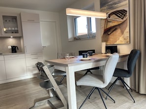 A modern dining area with a wooden table, grey upholstered chairs, and a painting of a boat on the wall. - Dahmer Dünen - Küstenkönigin - Dahmer Dünen "küstenkönigin " - Strand- und Zentrumsnah! (Dahme)