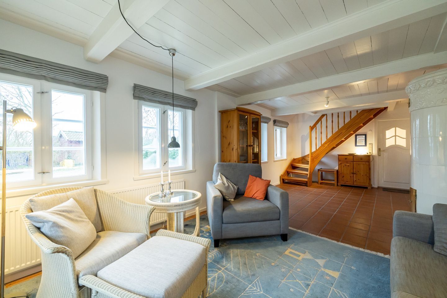 A spacious living room with a grey sofa, a round side table, and a blue patterned rug. There is a wooden staircase leading to an upper level.