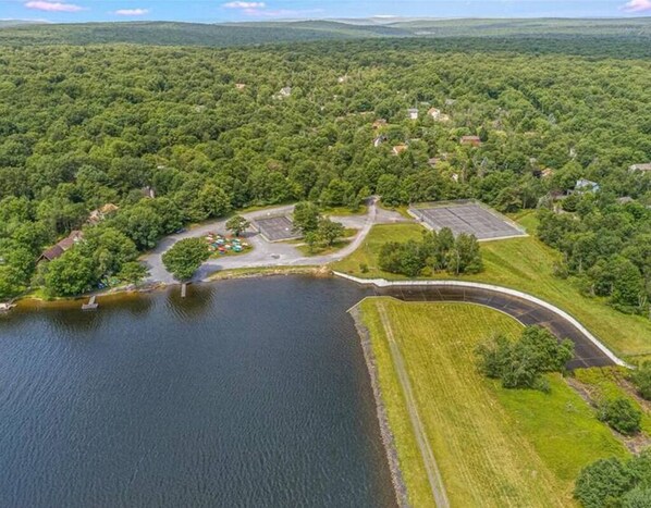An aerial view of a lakeside property with a parking area, a small dock, and a grassy embankment.