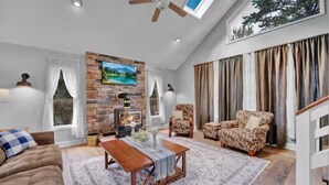 A spacious living room with a fireplace, a ceiling fan, and a large window with curtains. - The Easy St Chalet in Albrightsville (Albrightsville)