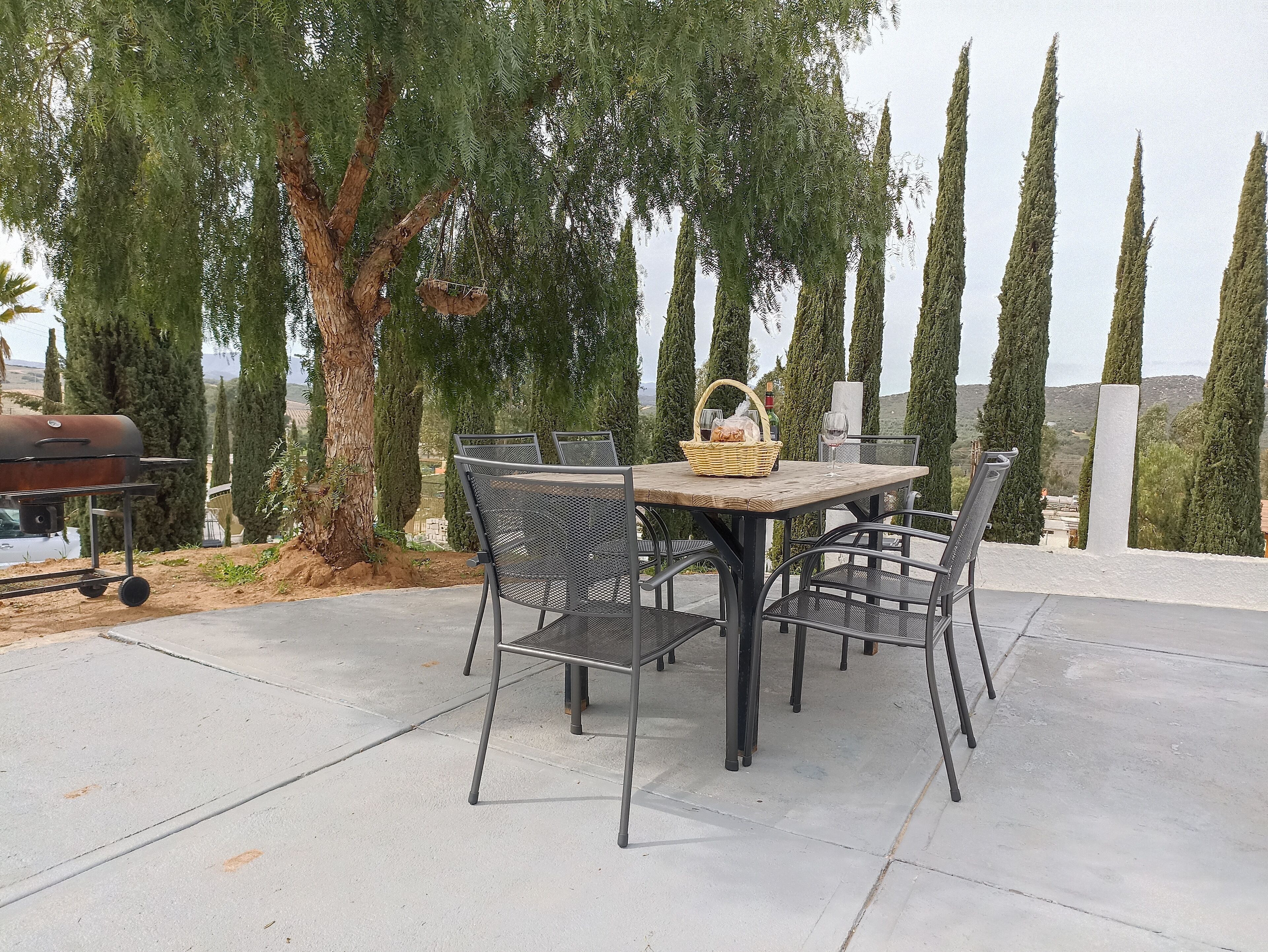 An outdoor patio with a round table and four chairs, a wicker basket, and a wine glass.