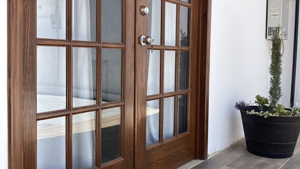 A wooden double door with glass panels, a potted plant, and a tiled floor. - Casa Ciprés (Valle de Guadalupe)