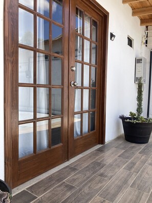 A wooden double door with glass panels, a potted plant, and a tiled floor. - Casa Ciprés (Valle de Guadalupe)