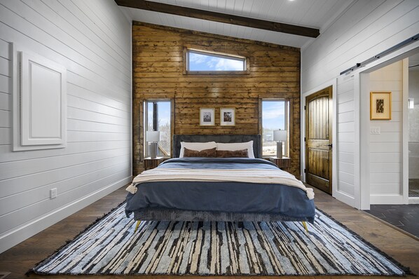 A bedroom with a large bed, wooden panel walls, a skylight, and framed pictures on the wall. - Couples, Hot Tub, Fire Pit, Pet Friendly, Peace & Quiet (Broken Bow)