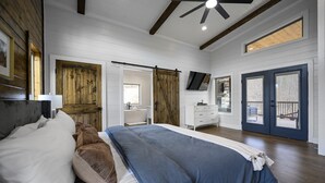 Une chambre avec un grand lit, des murs en bois, un ventilateur de plafond, une salle de bain avec un miroir et une porte donnant sur l’extérieur.