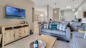 Una sala de estar moderna con un televisor de pantalla plana, mueble de entretenimiento de madera, sofá gris y un área de comedor al fondo.