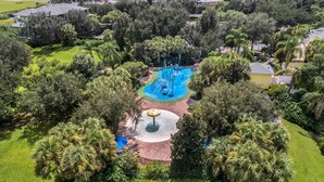 Vista aérea de una zona residencial con una fuente central rodeada de exuberante vegetación y palmeras.