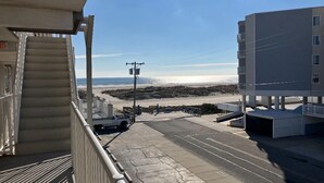 Vista desde un balcón sobre una playa, con un estacionamiento y un edificio al fondo.
