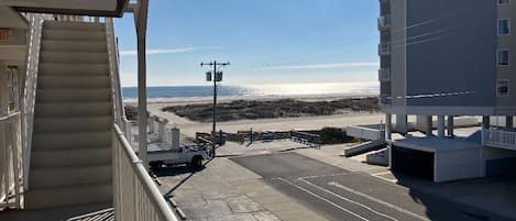 A view from a balcony overlooking a beach with a parking area and a building in the background.