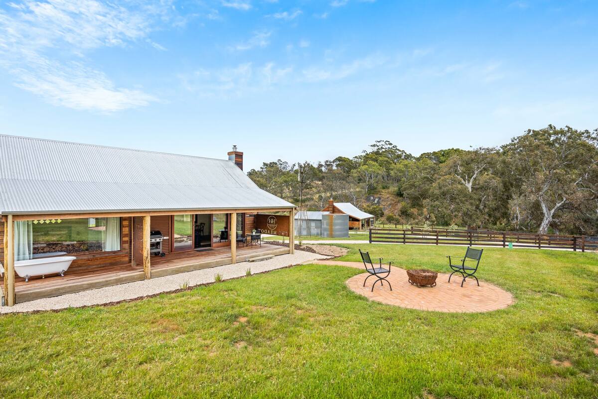 A modern house with a covered porch, a barbecue area, and a circular seating area with a fire pit.