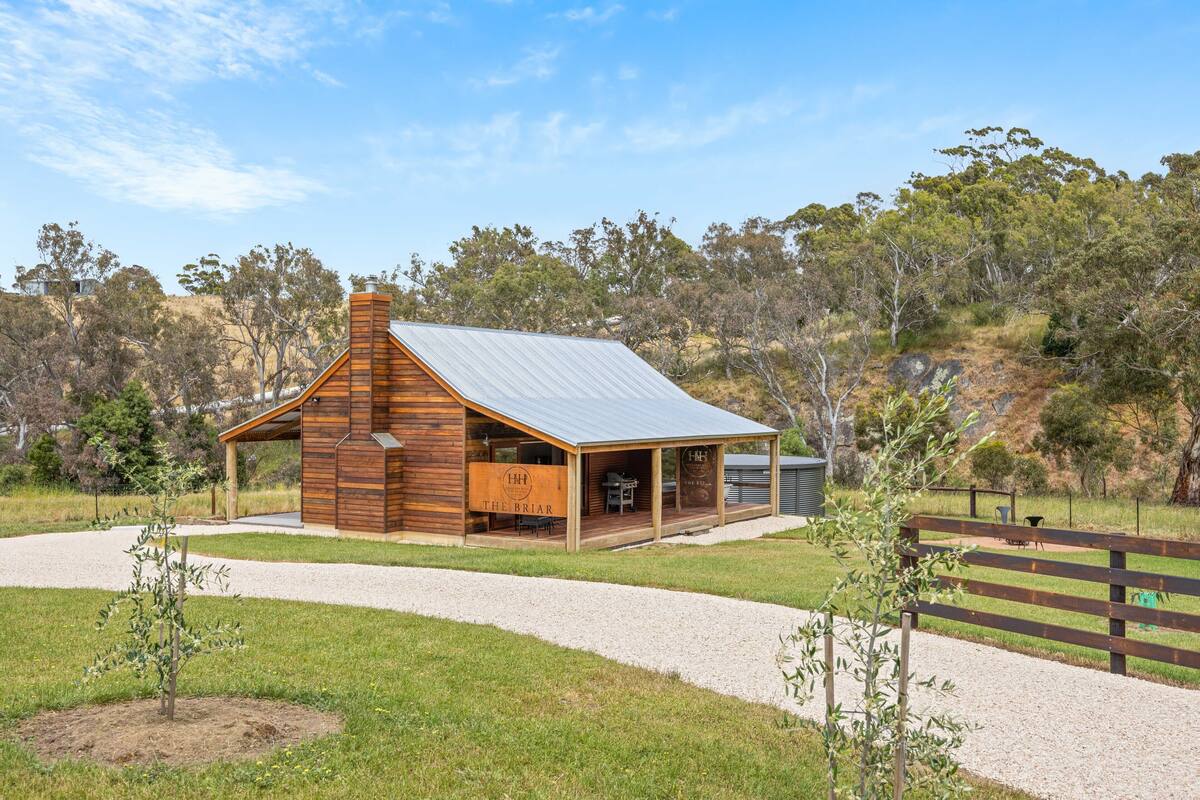 A rustic wooden building with a metal roof, a covered patio, and a gravel driveway.