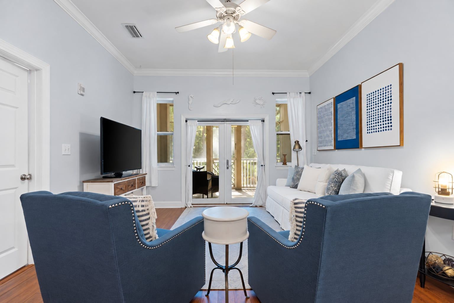 A living room with a television, two blue armchairs, a white sofa, and a ceiling fan.