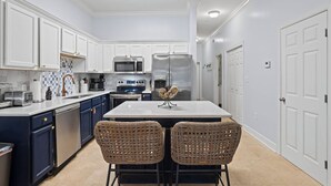 Une cuisine moderne avec des meubles blancs, des appareils en acier inoxydable et un îlot central agrémenté de chaises en osier.