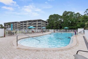 A swimming pool with lounge chairs and umbrellas, surrounded by a building with multiple balconies.
