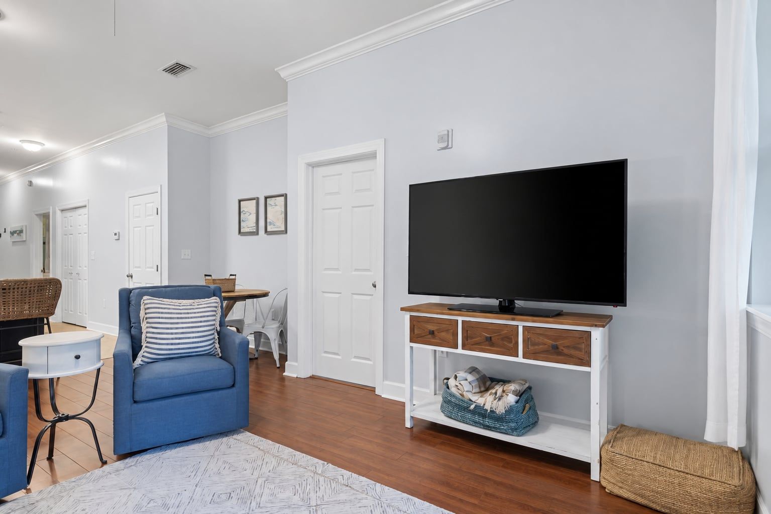 A living room with a flat-screen TV, a blue sofa, a small table, and a wicker basket.