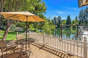 Une terrasse avec une table et des chaises, un parasol jaune et une vue sur un lac, visible à travers une clôture blanche.