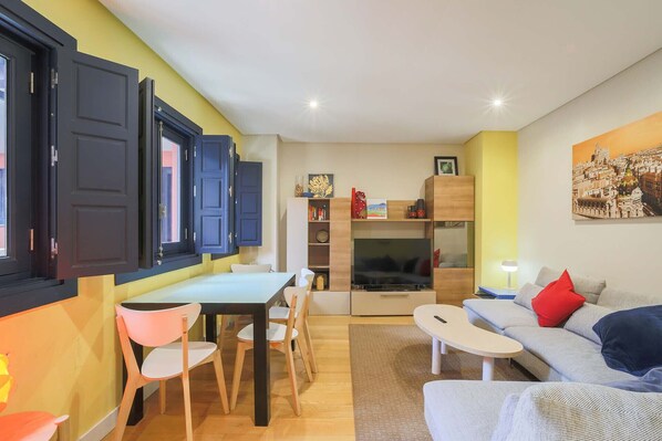 Una sala de estar acogedora con un sofá, una mesa de comedor con sillas, un televisor y una estantería.