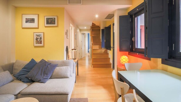 Una sala de estar con sofá, una mesa de comedor y una escalera que conduce a otro nivel.