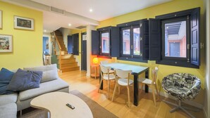 Un salón luminoso con un sofá, una mesa de comedor con sillas y una silla con temática de cómics.