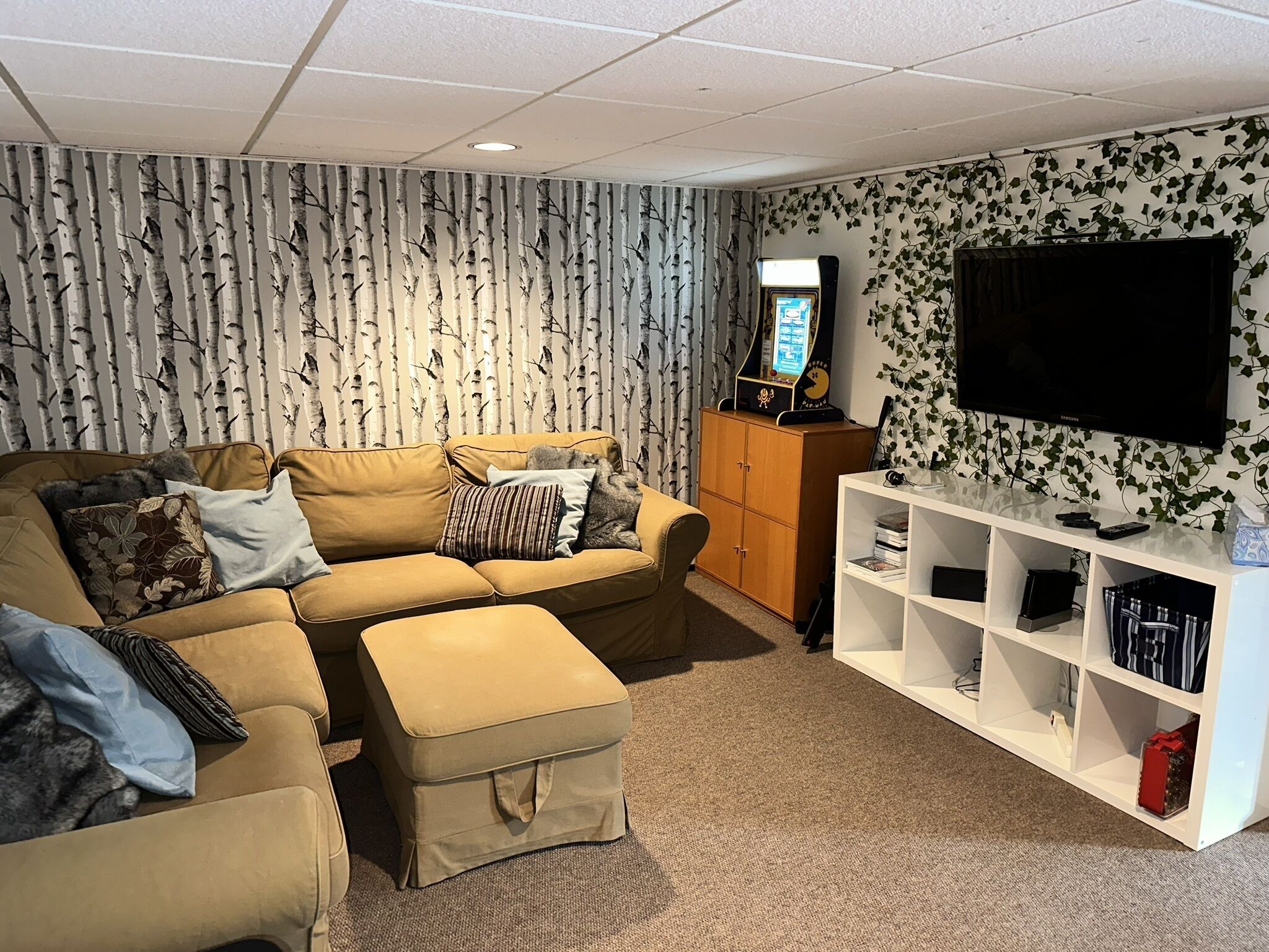 Een woonkamer met een bank, poef en een witte entertainmentkast.