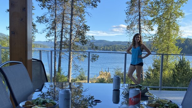 A dining table with meals and drinks, overlooking a lake with trees and hills in the background.