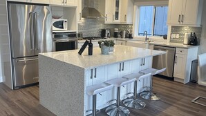 A modern kitchen with white cabinetry, stainless steel appliances, and a central island with bar stools.