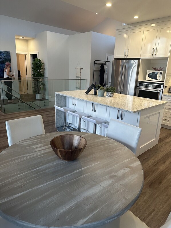 A modern kitchen with white cabinets, stainless steel appliances, and a granite countertop. - Luxury Lakeside House with large outdoor sauna (Shawnigan Lake)