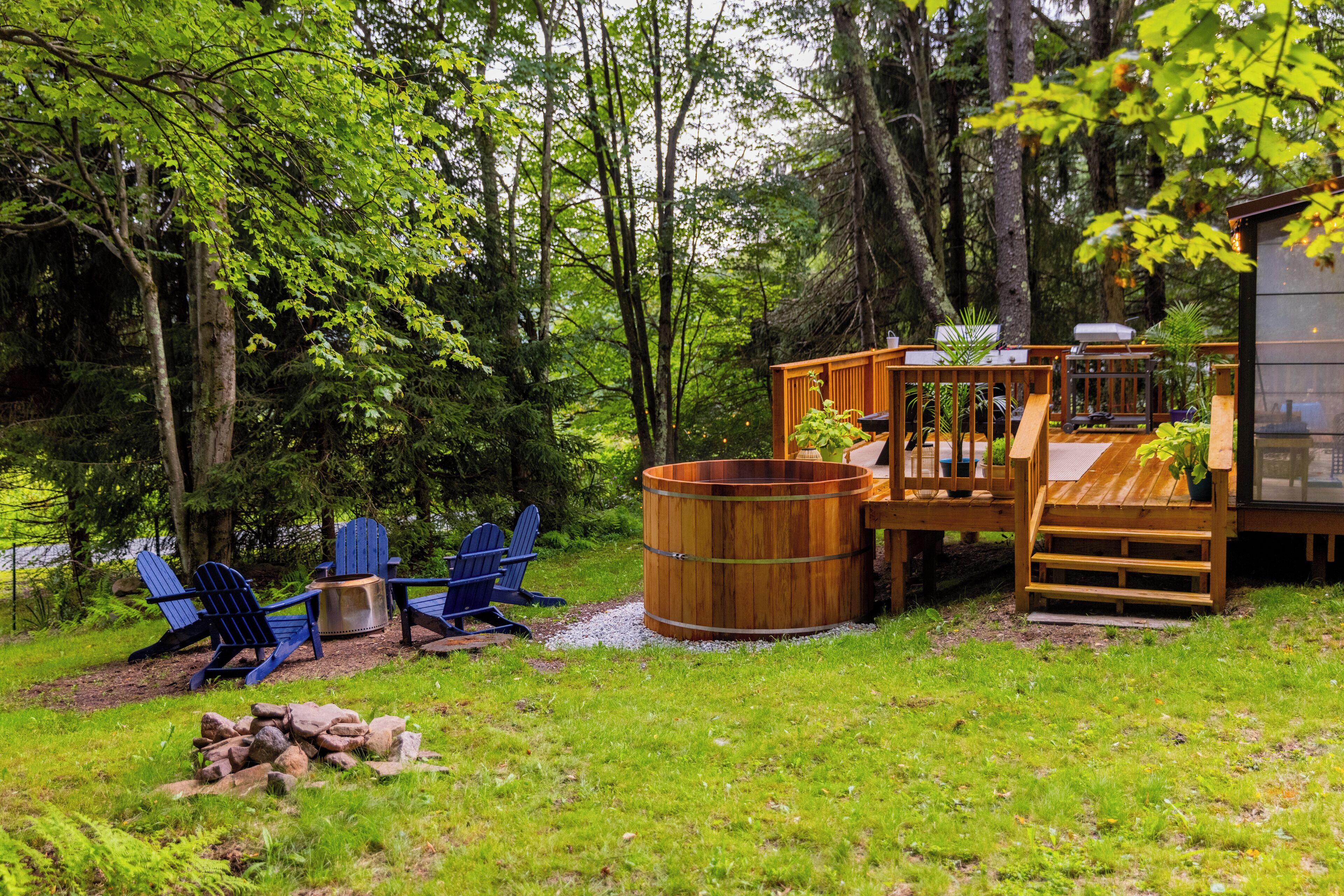 Une terrasse en bois avec un jacuzzi, des fauteuils Adirondack bleus et une petite structure ressemblant à un chalet.