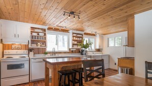 A cabin-style kitchen with wooden cabinets, a central island, and a dining area. - Waterfront Cottage on the Lake with Game Room & Sunroom (Lakefield)