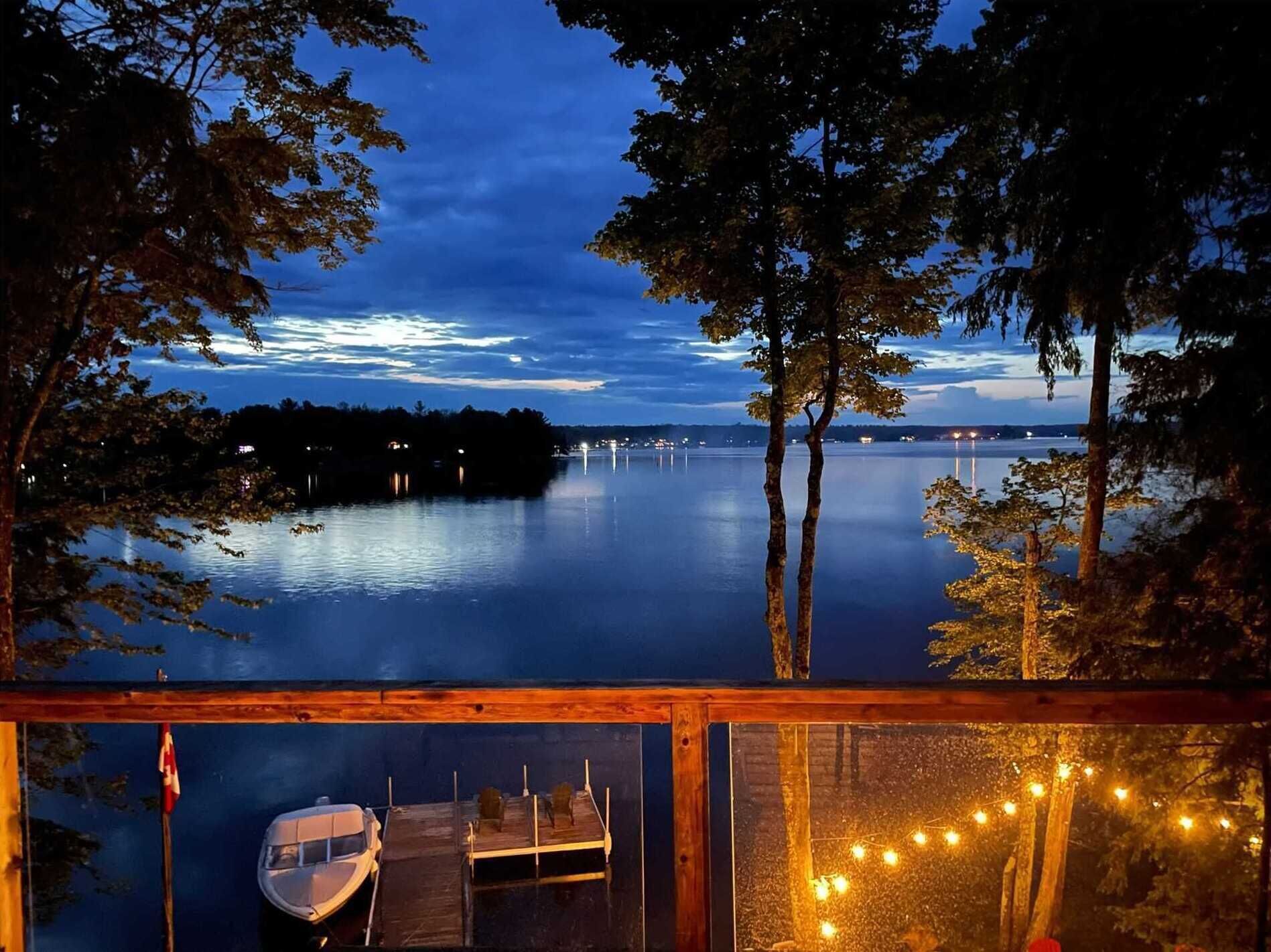 A lakeside cabin with a dock, a boat, and string lights.
