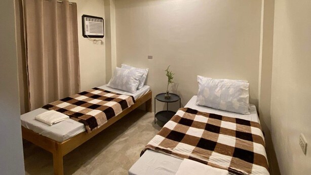 A small, clean room with two single beds, a small table, and a ceiling light. - Antelmi Inn (Plaridel)