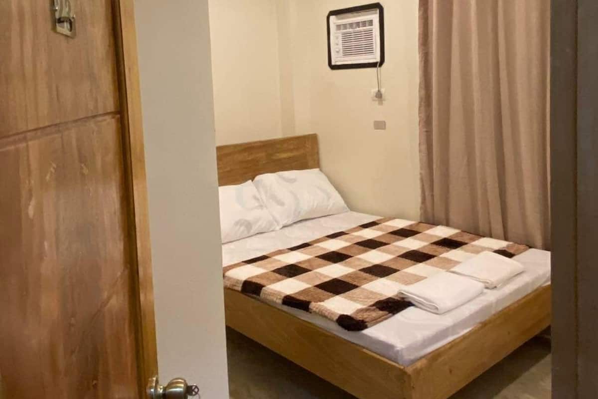 A bedroom with a wooden bed, a ceiling light, a wall-mounted air conditioner, and a door with a key lock.