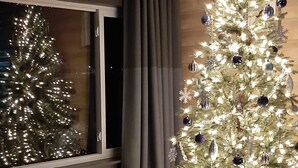A room with a large window, a bench, and a Christmas tree with lights and ornaments. - Cozy Beachfront Cottage (North Bay)