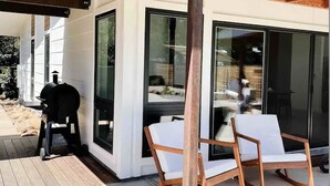 Une terrasse extérieure moderne avec une plateforme en bois, un barbecue et deux chaises blanches rembourrées.