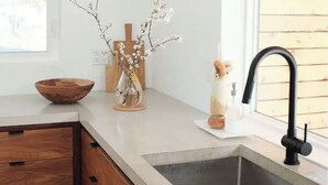 Une cuisine moderne avec des meubles en bois, un saladier posé sur le plan de travail, un vase avec des branches et un robinet.