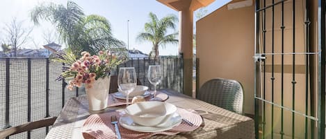 A balcony table set with plates, glasses, and a vase of flowers.