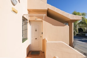 A beige exterior wall with a white door, a small window with bars, and a metal gate. - EL DESEO - Wonderful apartment with shared pool in Chiclana de la Frontera. (Chiclana de la Frontera)