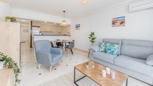 A modern living room with a grey sofa, a wooden coffee table, and a dining area with a table and chairs. - Lake view apartment with 1 bedroom and community pool (Empuriabrava)