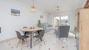 A modern living room with a dining area, featuring a round table, chairs, a sofa, and a view of the city through large windows. - Lake view apartment with 1 bedroom and community pool (Empuriabrava)