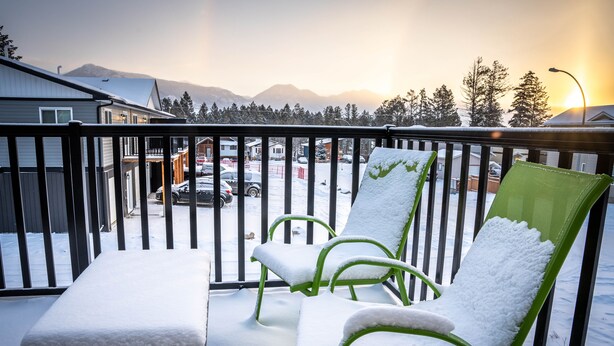 Ein Balkon mit schneebedeckten Stühlen und einem Tisch, mit Blick auf eine verschneite Straße und Berge.