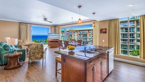 A spacious living area with a large island, a dining table, and a view of a hotel building. - Maui Resort Rentals: Honua Kai Konea 609/13 - 4 Total Bedrooms, 6th Floor Deluxe Ocean Views! (Lahaina)