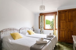 A room with two beds, a window with curtains, a wooden wardrobe, and a hanging light fixture. - 3 bedroom country house with private pool and barbecue (Pollensa)