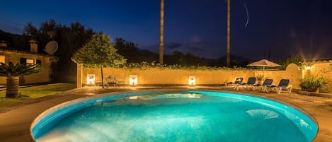 A swimming pool with lounge chairs and a table, surrounded by palm trees and a building with satellite dishes.
