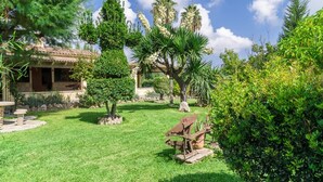 A well-maintained garden with a variety of trees and shrubs, a stone patio, and a rustic wooden structure. - 3 bedroom country house with private pool and barbecue (Pollensa)