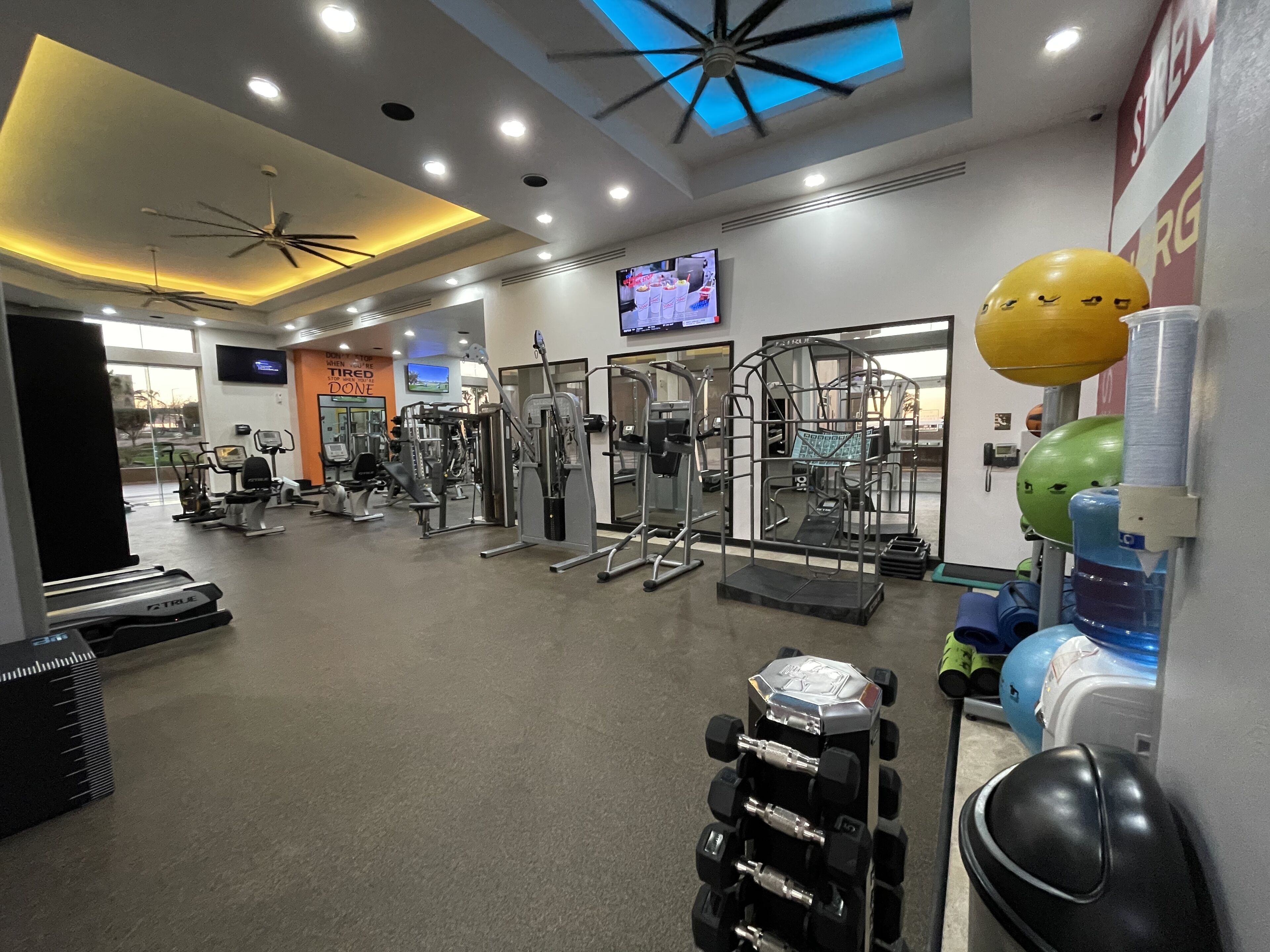 Ein Fitnessraum mit Trainingsgeräten, einem Fernseher und einem Deckenventilator.