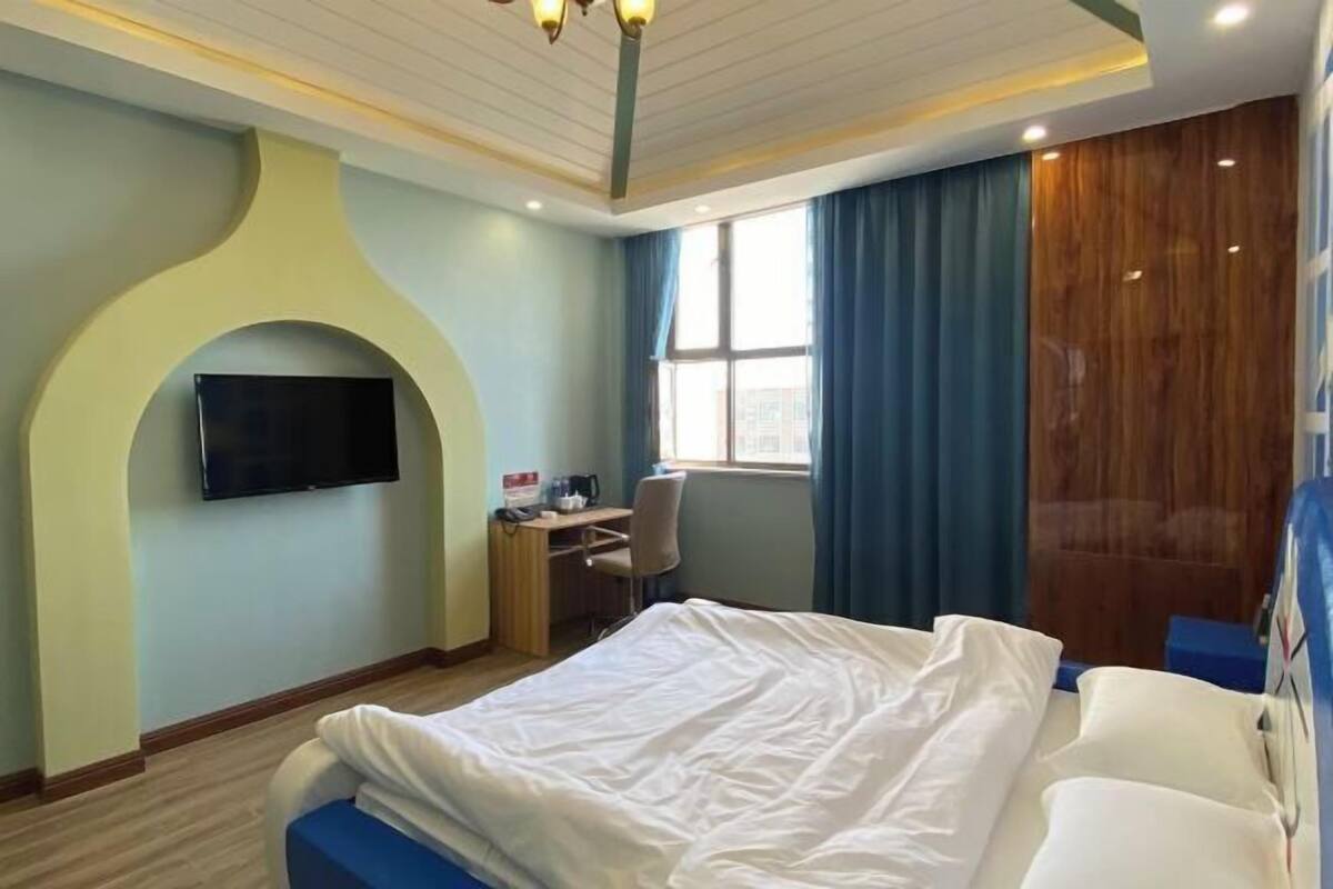 Une chambre d’hôtel comprenant un lit, un bureau avec une chaise, un téléviseur à écran plat fixé au mur et une fenêtre avec des rideaux.