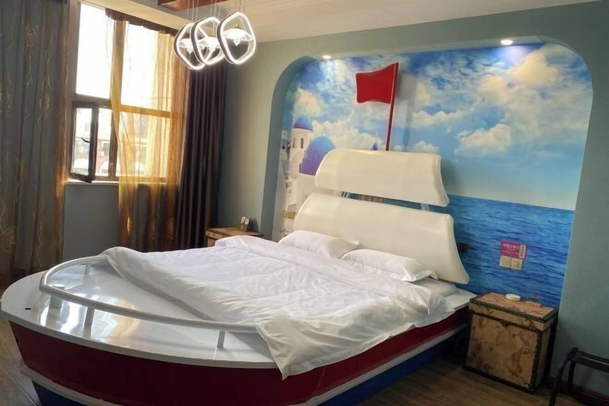 Une chambre dotée d’un lit avec une tête de lit en forme de bateau, d’une fresque représentant un voilier sur le mur et d’une fenêtre avec des rideaux.